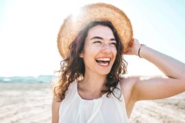 A woman wearing a sun hat while standing and smiling at a beach